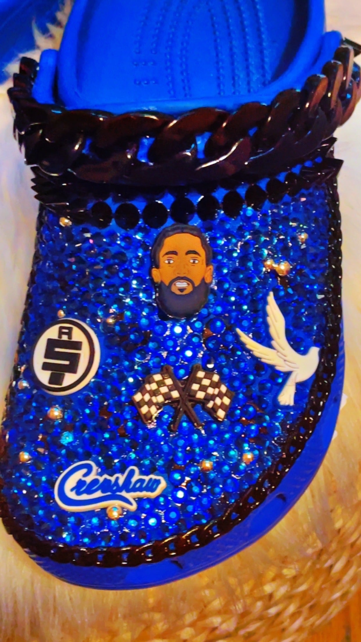 Step into Nipsey Hussle's legacy with our Blue Crocs. Featuring a Nipsey Hussle patch and iconic Jibbitz, these Crocs pay homage to the legendary artist. The sleek blue design and chic black accents add urban style to comfort. 🎵👟🌟 #NipseyHussle #CustomCrocs #FashionFootwear - Left Foot