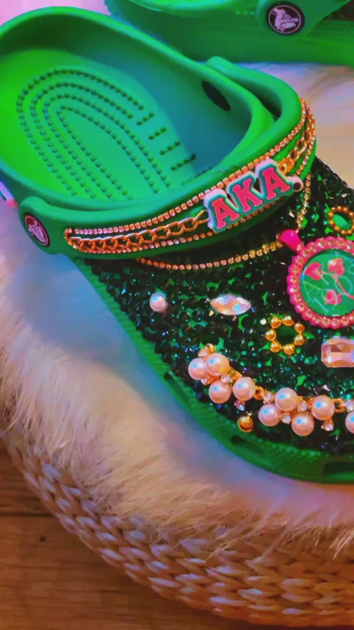 Step into sisterhood with our AKA Sorority Inspired Crocs: vibrant green, sparkling rhinestones, elegant pearls, lavish gold, and chic pink accents. A tribute to unity and style. 💚👡🌟 #SororityPride #Fashion